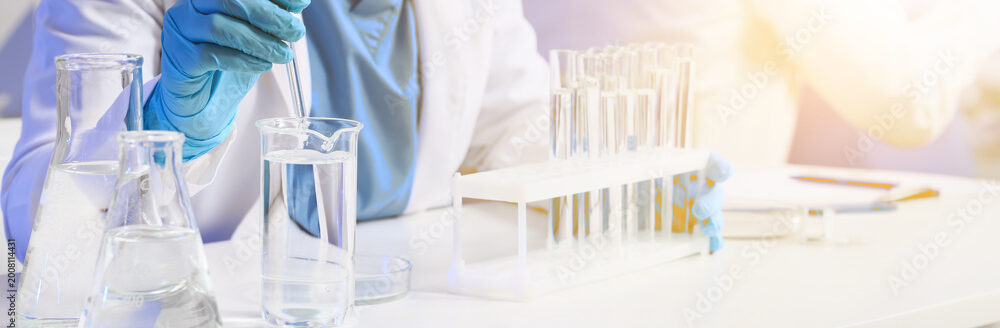 A lab technician uses a pipette to move liquid from a beaker to a tray of test tubes in an ISO 17025 accredited laboratory