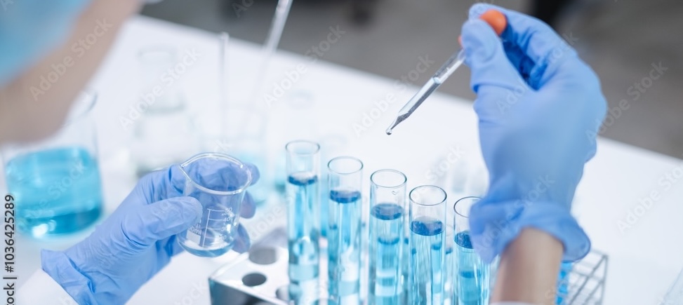 A lab technician's gloved hands add a drop of solution to a row of test tube samples to identify active ingredients