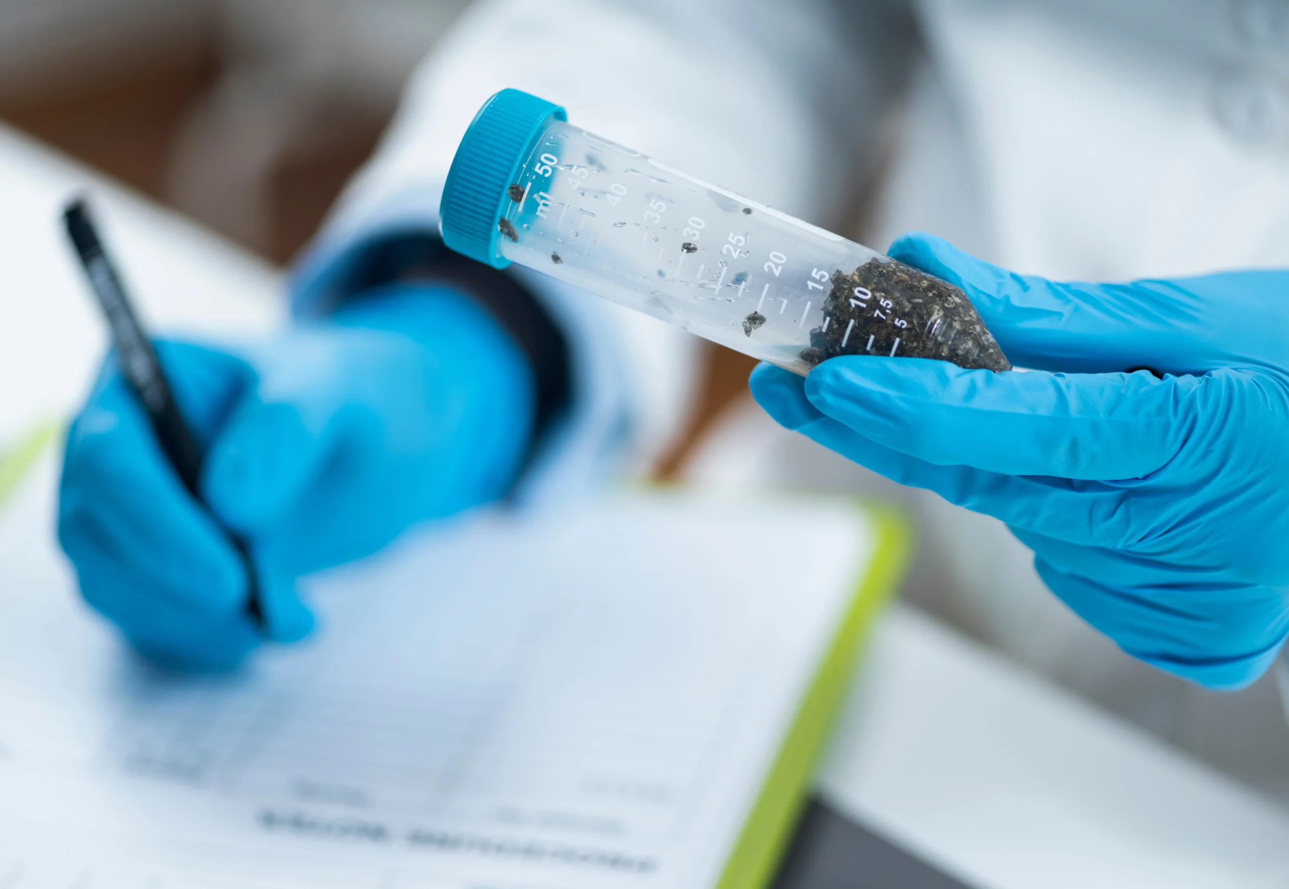 Scientist wearing blue gloves holding a laboratory tube containing a soil sample for environmental analysis.