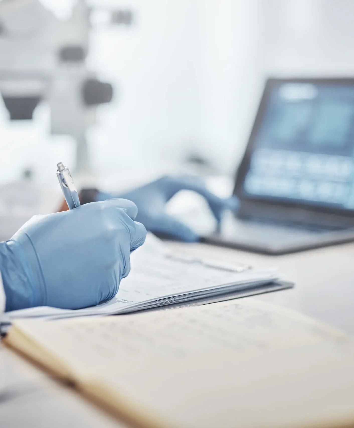 Testing lab professional in blue gloves writing notes at a laboratory workstation with a computer in the background.