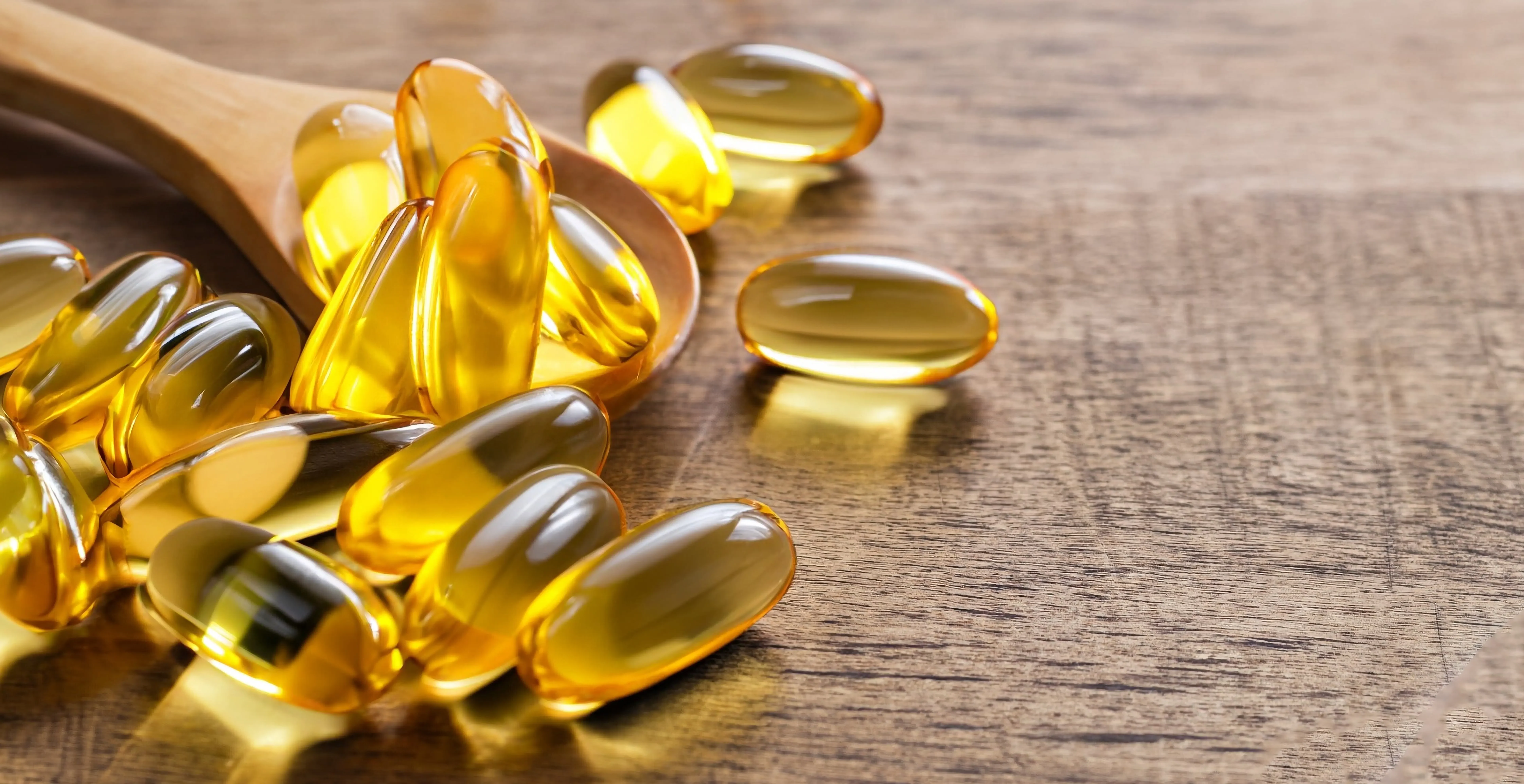 Golden fish oil supplement capsules arranged on a wooden spoon and surface, representing omega-3 nutritional supplements.