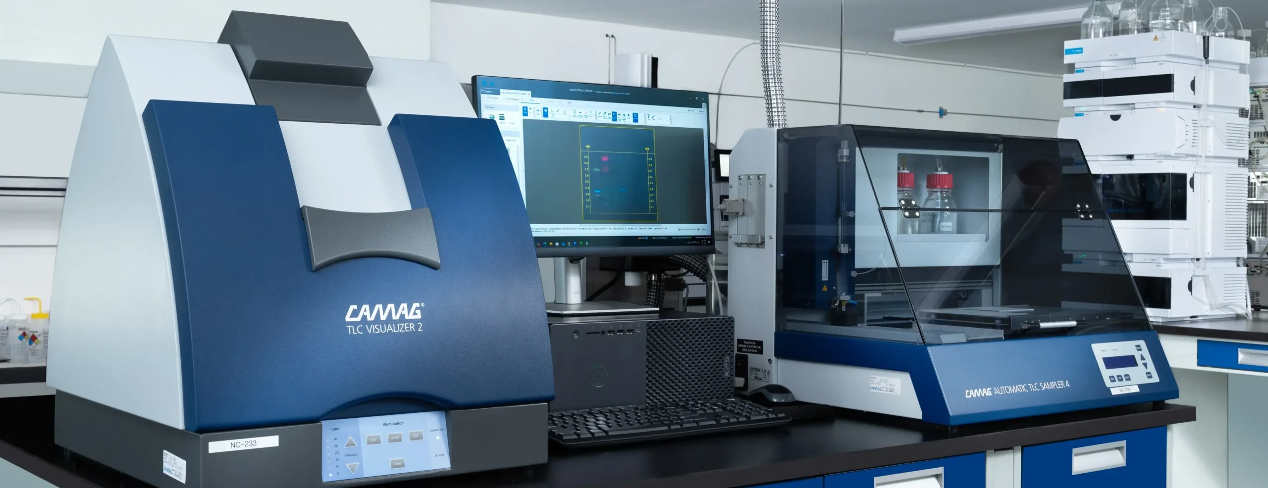 Advanced laboratory with TLC visualization equipment, automated sample analyzer, computer monitor, and analytical testing instruments.